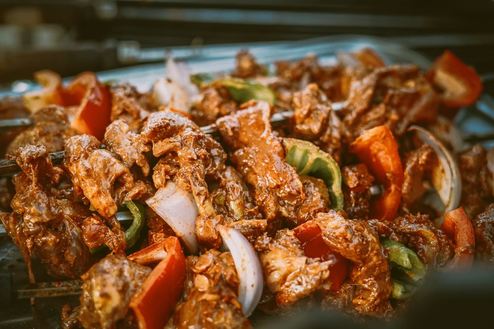 Close-up of skewers laid across a grill — spiced beef threaded with red pepper, green pepper and onion, glistening with yaji-thickened marinade.